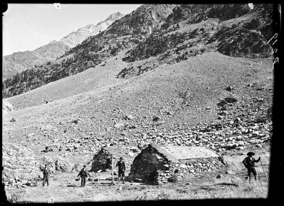 Grup d'homes al costat d'unes cabanes de pedra a la pleta del Calcilé en una planura entre muntanyes