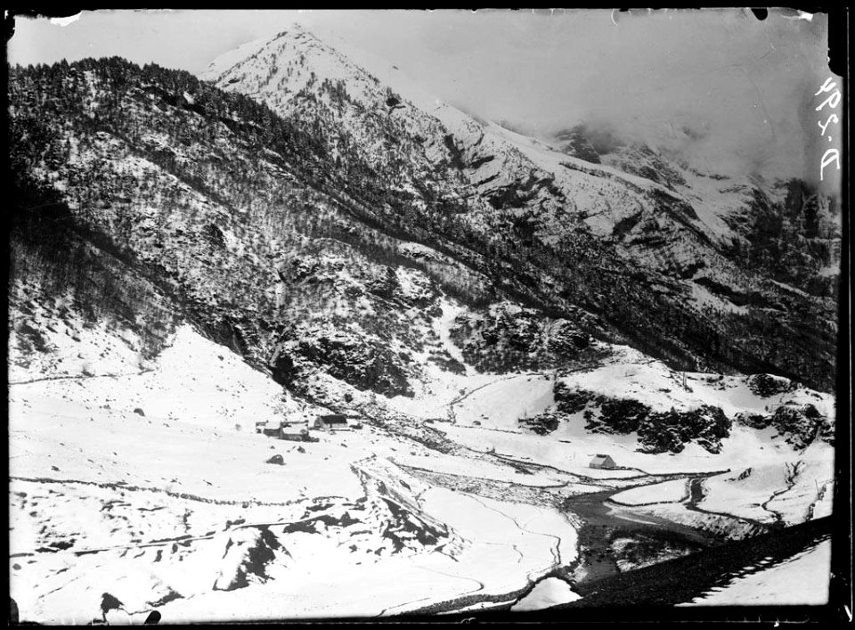 Grup de cases i riu en una vall nevada voltada de boscos