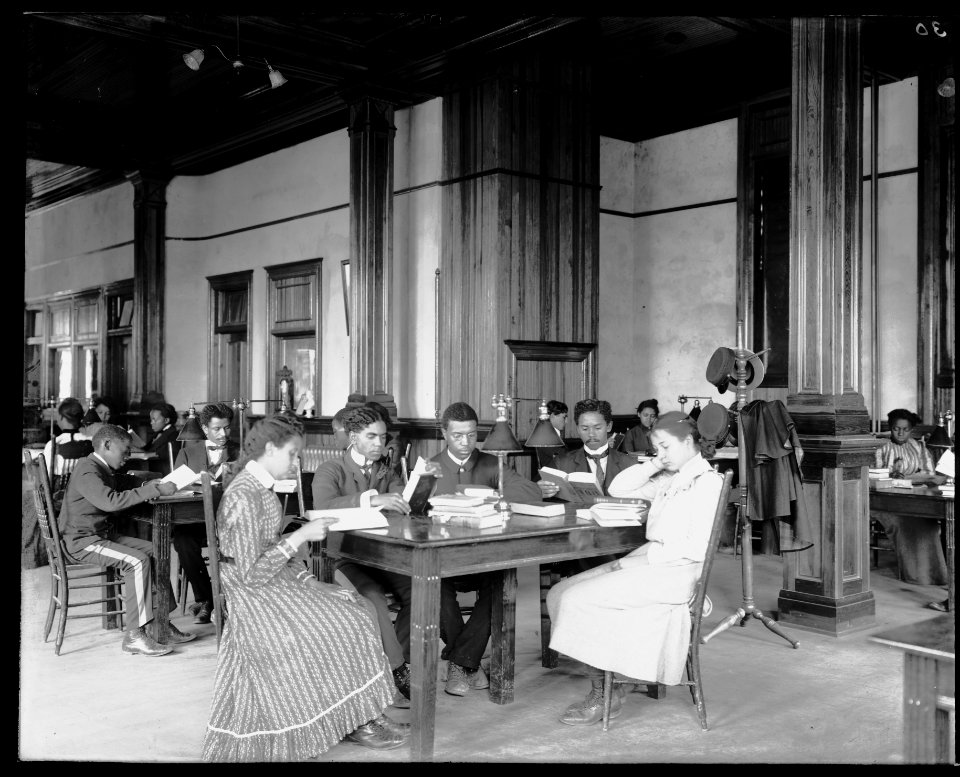 Interior view of library reading room with male and female students sitting at tables, reading, at the Tuskegee Institute LCCN2009632000