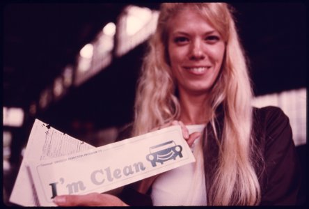 Happy Young Woman with a Bumper Sticker Which Reports She Had Successfully Passed Testing at an Auto Emission Inspection Station in Downtown Cincinnati, Ohio...09-1975 (4265799845)