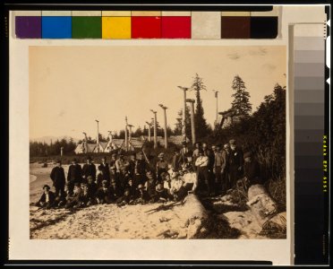 Harriman Alaska Expedition members pose on beach at deserted Cape Fox village, Alaska, 1899, with Tlinget totem poles in background) - Curtis LCCN00649757