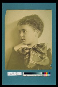Head-and-shoulders portrait of a young boy with a large plaid bow at the neck of his jacket, facing left LCCN2004676298