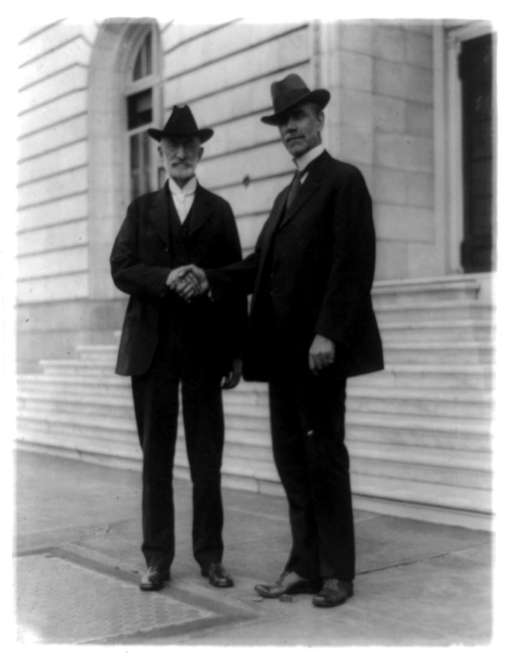 Heber Jeddy Grant (1856-1945) left, standing and shaking hands with Reed Smoot (1862-1941) outside Senate office building LCCN91786784