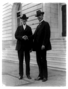Heber Jeddy Grant (1856-1945) left, standing and shaking hands with Reed Smoot (1862-1941) outside Senate office building LCCN91786784