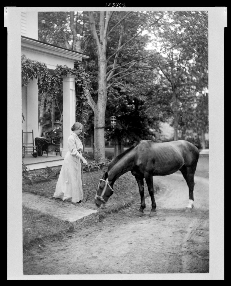 Helen Keller, full-length portrait standing on lawn holding reins to a horse LCCN99471717