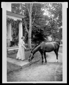 Helen Keller, full-length portrait standing on lawn holding reins to a horse LCCN99471717