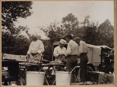 Henry Ford and Harvey Firestone assisting two chefs by peeling potatos at a Ford-Edison camping trip LCCN2011645209