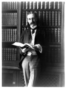 Herbert Putnam, three-quarter-length portrait, standing, facing left, in library, holding book LCCN96507335