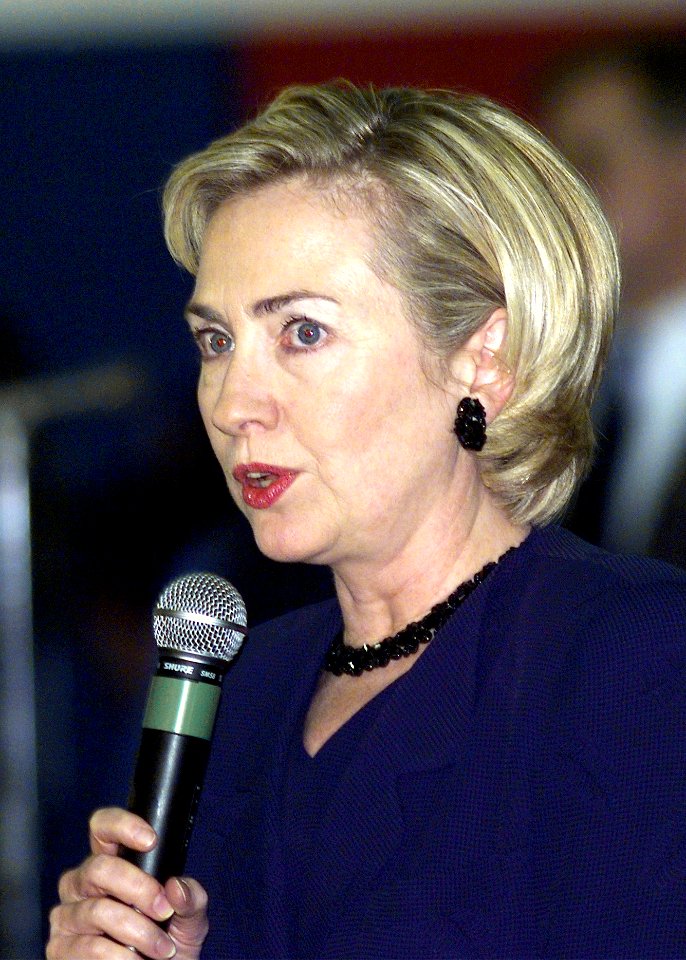 Hillary Rodham Clinton speaks over a microphone to the assembled Kosovo refugees