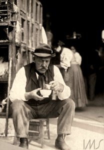 Homem sentado, comendo, próximo à gaiolas com galinhas - Vincenzo Pastore photo