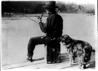 Hooch Hound, a dog trained to detect liquor (as suggested to Commissioner Haynes by a prohibition agent in Colorado), sniffs at flask in back pocket of man, seated, fishing on pier on the LCCN89707464