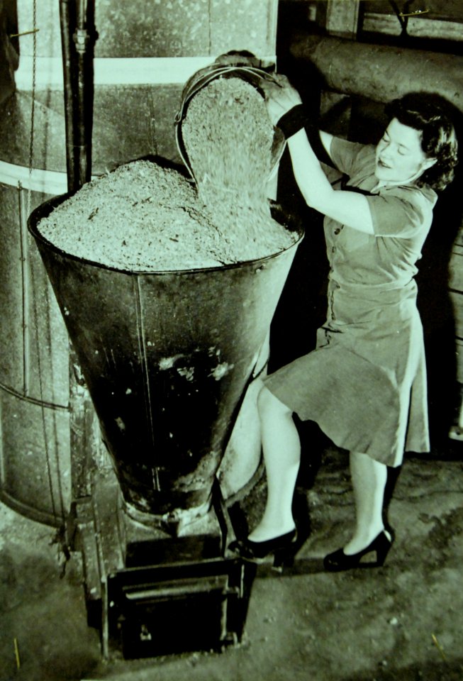 House wife is filling the hopper of the household sawdust burner, 1942 (23681690775)