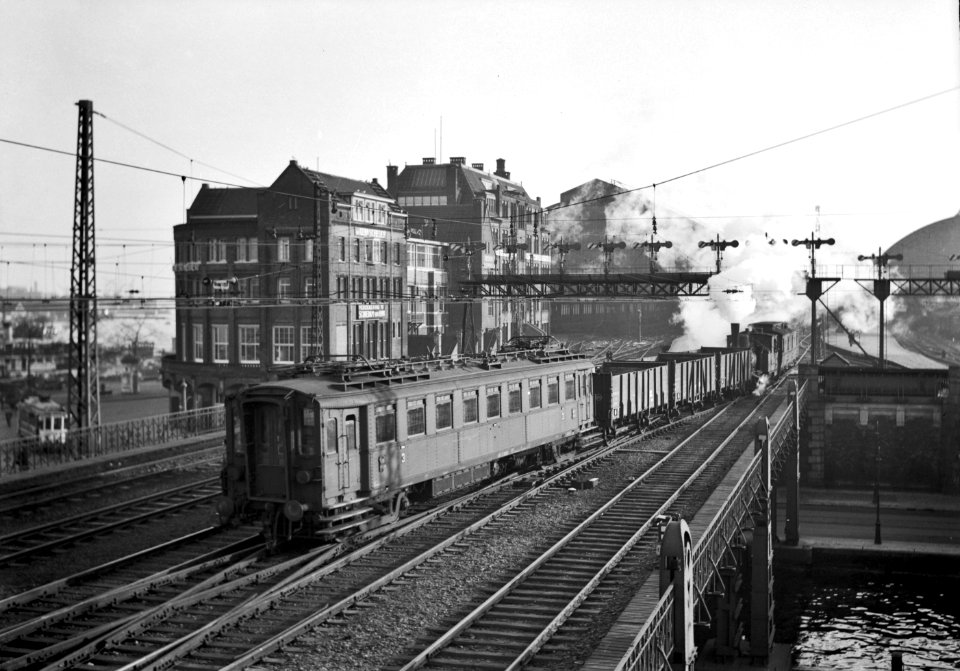 HUA-151658-Afbeelding van een rangeerdeel met voorop een rijtuig van het electrisch buffermaterieel ('blokkendozen, mat. 1924) van de N.S. op de brug over de Westertoegang bij het N.S.-station Amsterdam C.S. (westzijde) te Amsterdam