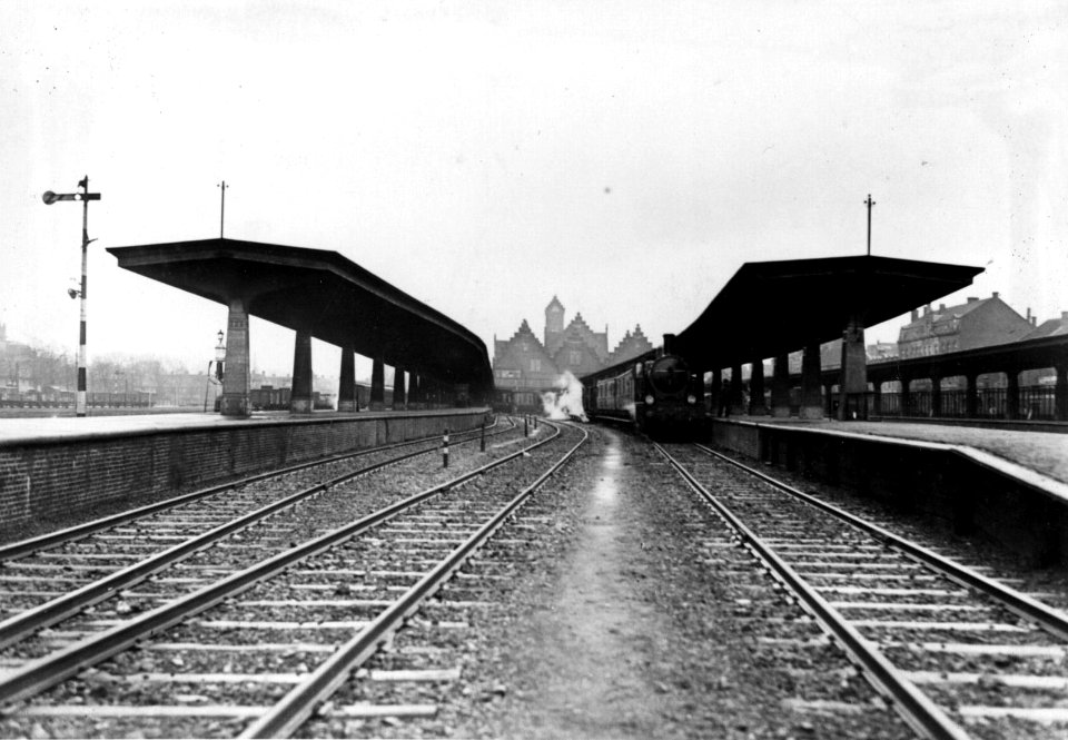 HUA-154645-Gezicht op de perrons en de perronkappen van het NS station Maastricht te Maastricht met op de achtergrond een stoomtrein en het stationsgebouw