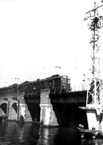 HUA-154927-Afbeelding vaneen trein bestaande uit ruituigen van het electrisch buffermaterieel (mat. 1924, Blokkendozen) van de N.S. op een spoorbrug bij het N.S.-station Amsterdam C.S. te Amsterdam