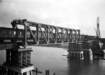 HUA-154934-Gezicht op de herstelde spoorbrug (noodbrug) over de Maas te Buggenum met een stoomtrein
