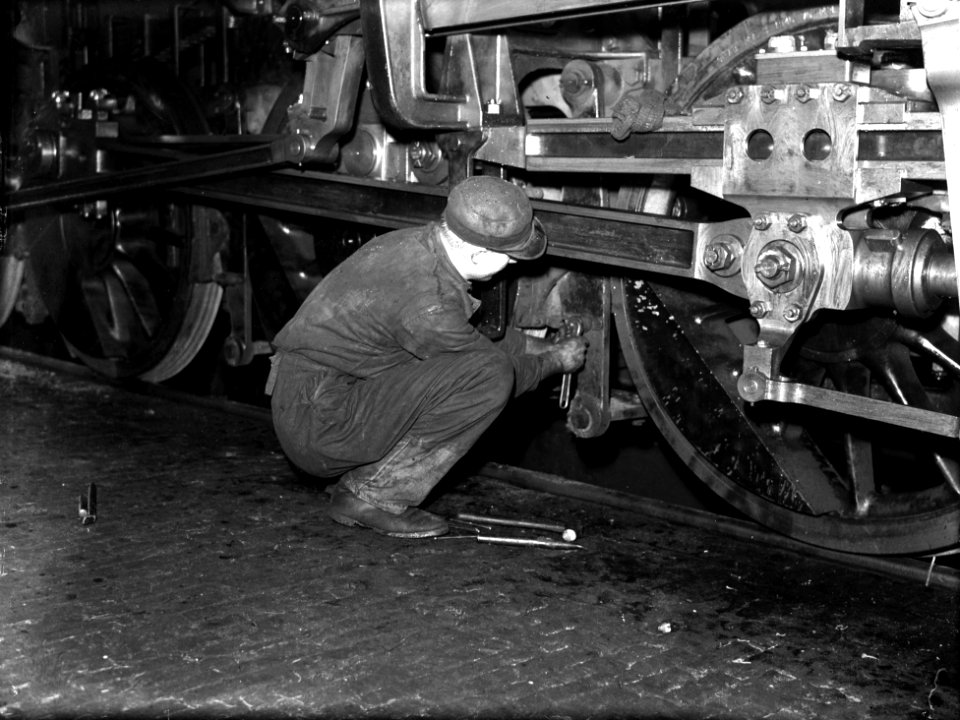 HUA-151466-Afbeelding van een monteur die onderhoud pleegt onder het loopwerk van een Zweedse 3 cilinder stoomlocomotief uit de serie 4700 van de N.S