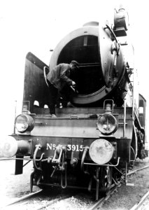 HUA-151485-Afbeelding van de voorzijde van de stoomlocomotief nr. 3915 (serie 3900) van de N.S. met op de locomotief personeel dat de rookkast reinigt