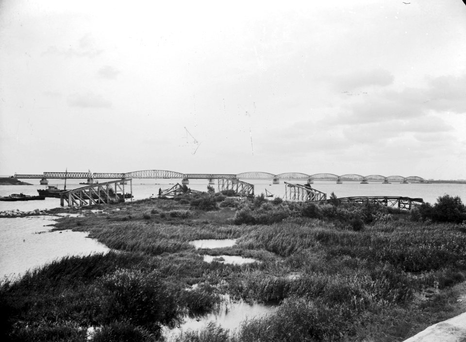 HUA-152684-Gezicht op de van oorlogsschade herstelde spoorbrug over het Hollands Diep bij Moerdijk. Op de voorgrond liggen restanten van vernielde brugdelen