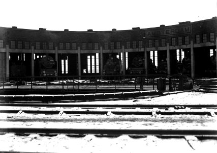 HUA-163295-Gezicht op de locomotiefloods bij het N.S.-station Amsterdam C.S. te Amsterdam, met diverse stoomlocomotieven en op de voorgrond de draaischijf