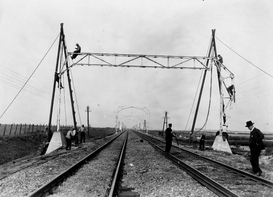 HUA-163424-Afbeelding van de plaatsing van een bovenleidingsportaal tijdens de electrificatie van de spoorlijn Schiedam Hoek van Holland