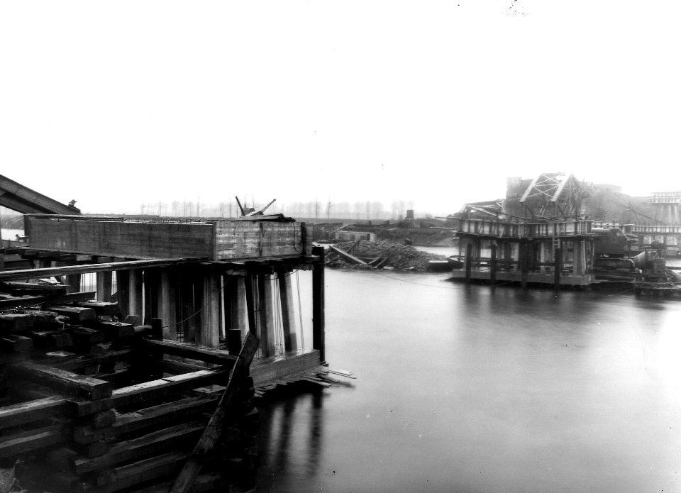 HUA-163517-Gezicht op de tijdens de oorlog vernielde spoorbrug over de Maas bij Buggenum, met de noodpijlers voor de te bouwen hulpbrug