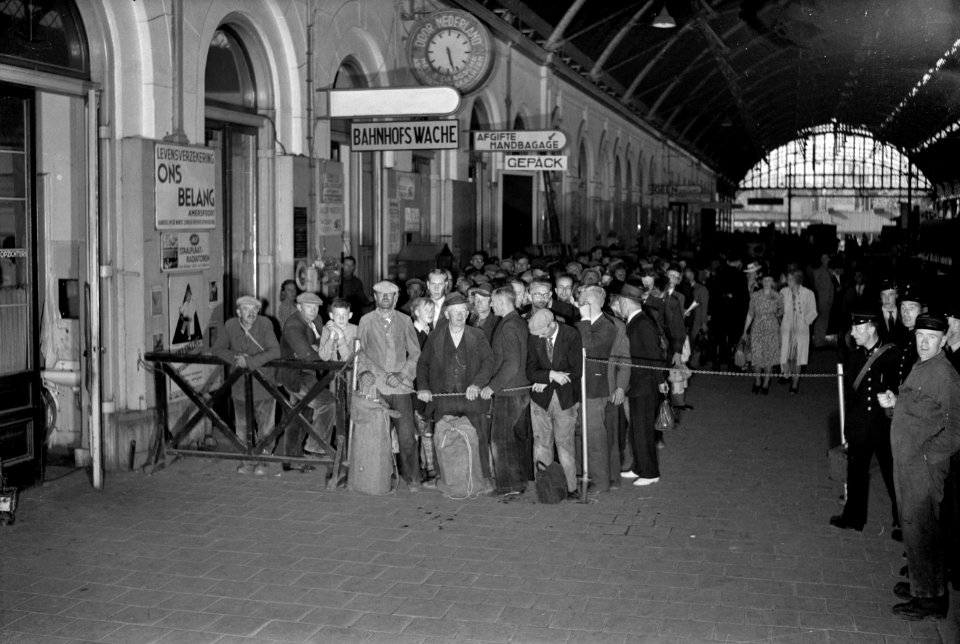 HUA-154621-Afbeelding van een menigte reizigers bij de in of uitgangscontrole op het perron van het NS station Den Haag SS met Duitse bebordingen te Den Haag