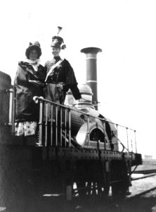 HUA-163743-Afbeelding van twee gekostumeerde personen op de replica van de stoomlocomotief De Arend van de N.S., vermoedelijk te Hoofddorp, in verband met filmopnamen