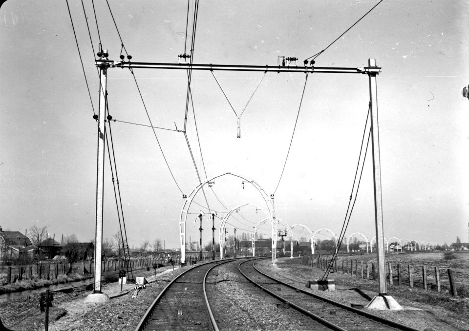 HUA-167144-Gezicht op de spoorlijn bij Groenekan, kort na de electrificatie, met op de voorgrond een bovenleidingsportaal van Differdinger profielen en daarachter de kenmerkende halfronde betonnen bovenleidingsp