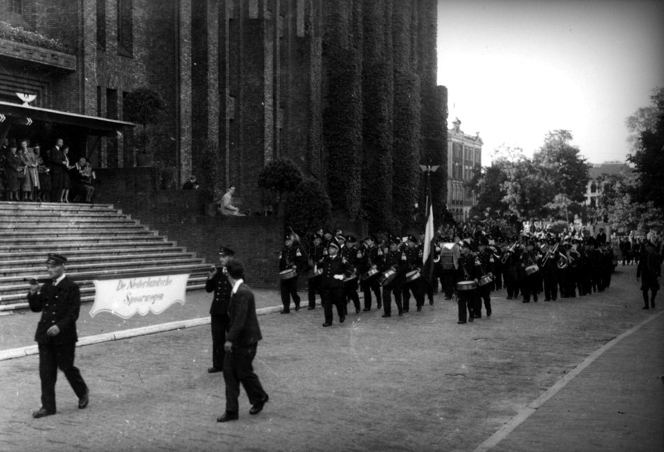HUA-160661-Afbeelding van het harmonieorkest van de N.S. tijdens een defilé langs het 3e Administratiegebouw van de Nederlandse Spoorwegen (HGB III, Moreelsepark) te Utrecht