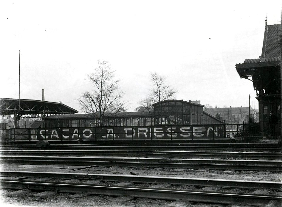 HUA-163180-Gezicht op de reclamebelettering (Cacao A. Driessen) op de balustrade van de dienstbrug tussen het Buurtstation aan het Leidseveer (links) en het stationspostkantoor te Utrecht