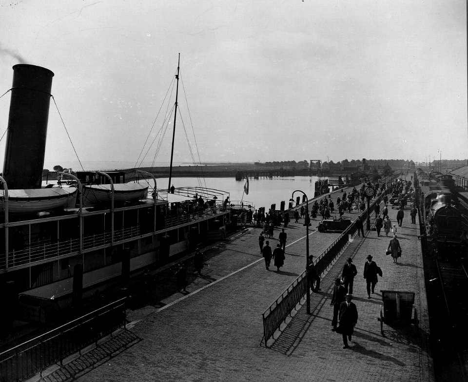 HUA-163216-Gezicht op de kade van de haven te Enkhuizen, met links de stoomboot van Rederij Koppe naar Stavoren en rechts het perron van het N.S.-station Enkhuizen met een juist aangekomen trein getrokken door d