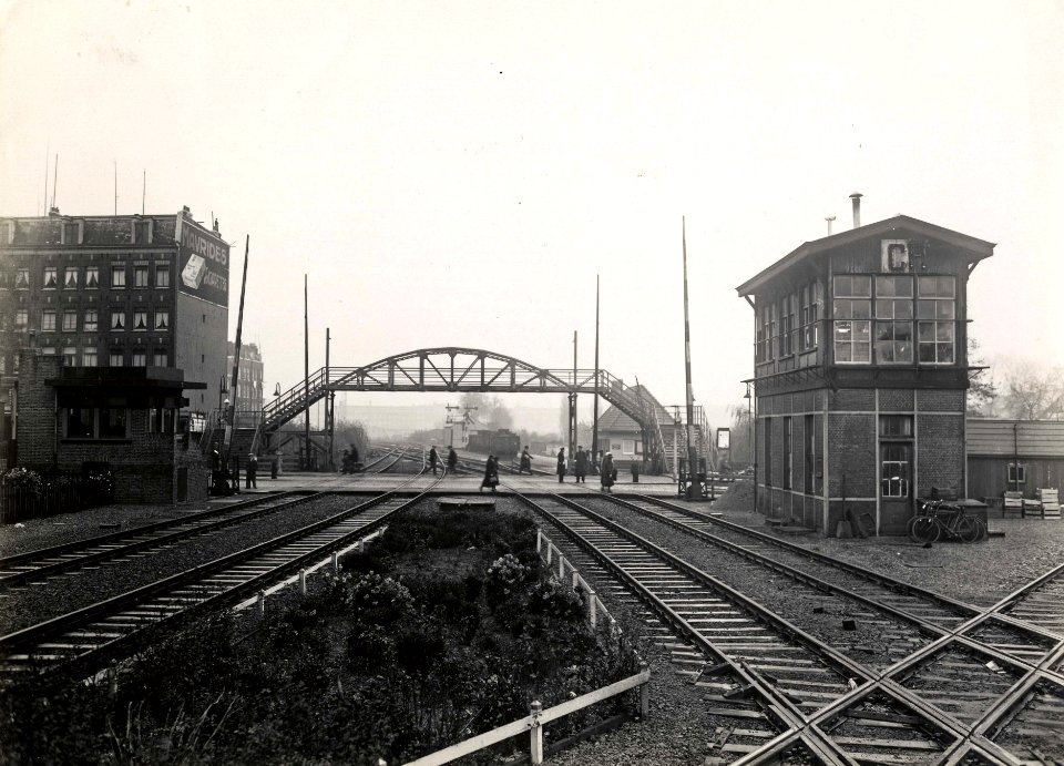 HUA-163661-Gezicht op de voetgangersbrug en spoorwegovergang in de Linnaeusstraat te Amsterdam, met links de overwegpost en rechts het seinhuis Post C. N.B. De afbeelding maakt deel uit van een serie foto's met 