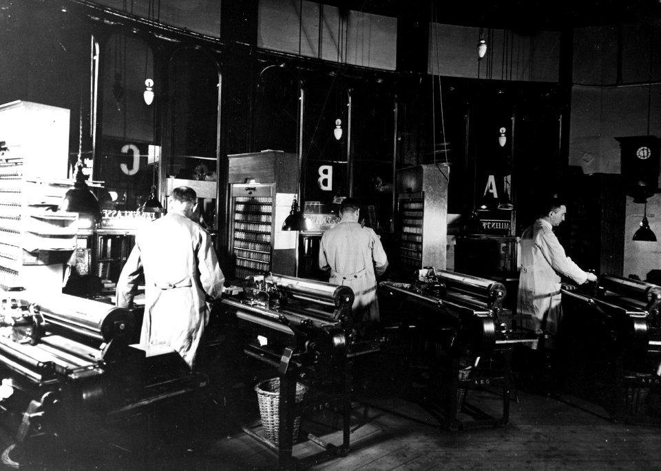 HUA-165641-Interieur van het N.S.-station Amsterdam C.S. te Amsterdam- plaatskaartenkantoor, met lokettisten en plaatskaartendrukmachines van het type Regina