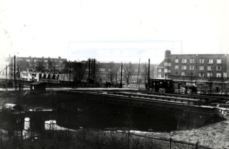 HUA-169353-Gezicht op het spoorwegovergang in de Linnaeuskade en de spoorbrug over de Noorderringvaart te Amsterdam, met de brugpost Wgw (Watergraafsmeer West). Op de achtergrond de huizen aan de Archimedesweg. 