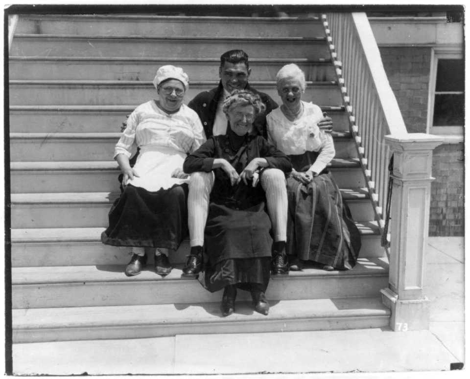 Jack Dempsey at his training camp, June 1921- hugging 3 old women on porch steps LCCN2005681069