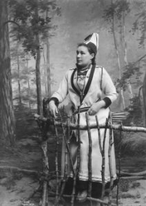 Kvinne i sørsamisk inspirert drakt holder i et gjerde - Norsk folkemuseum - NF.09522-003
