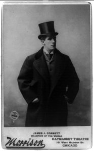 James John Corbett, three-quarter length portrait, standing, facing right, wearing overcoat and top hat LCCN96523836