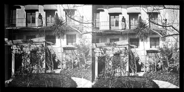 Jardí i façana d'una casa amb una dona en un balcó