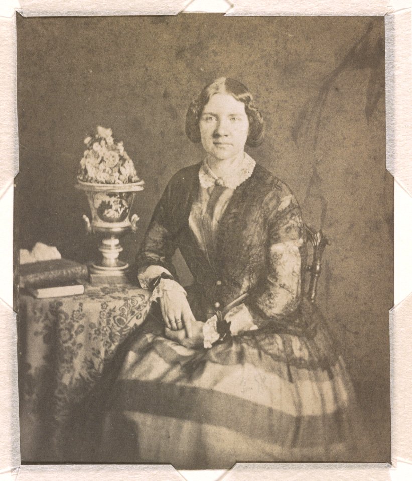 Jenny Lind, three-quarter length studio portrait, facing front, seated next to a table with her right arm resting on the table and left hand on her lap; there are books and a vase on the LCCN2015651566