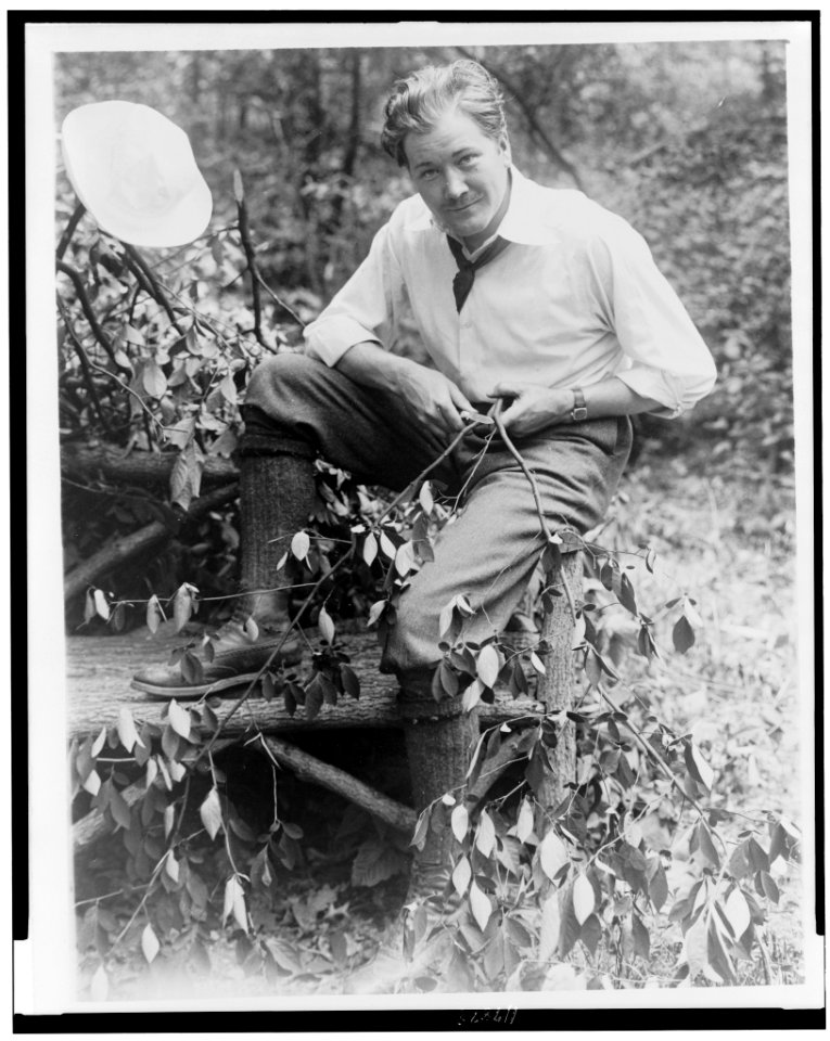 John Charles Thomas, singer, full-length portrait, sitting on log bench, whittling a small branch LCCN97509098
