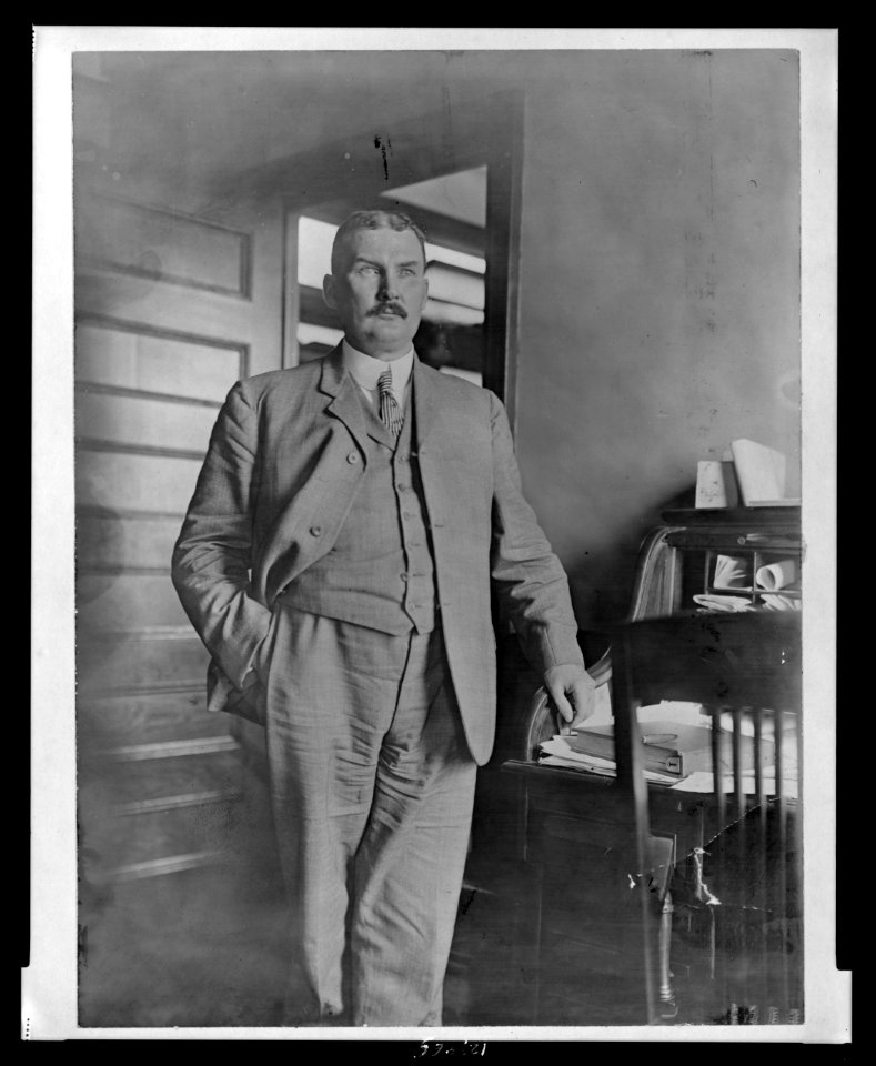 John Ford, three-quarter length portrait, standing, facing slightly right, with his left hand on rolltop desk LCCN99471942