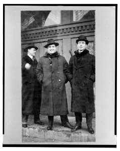 John McCormack, Irish-born American tenor, full-length portrait, facing front, standing with two men on steps outside building LCCN2004669706