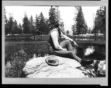 John Muir, full-length portrait, facing right, seated on rock with lake and trees in background LCCN95514008 photo