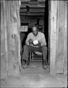 Joshua Spradley, miner, sitting in doorway of his two rooms in garage house. He pays $10.60 per month rent, includes... - NARA - 540936