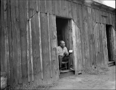 Joshua Spradley, miner, sitting in doorway of his rooms in garage house. He pays $10.60 monthly, includes... - NARA - 540935