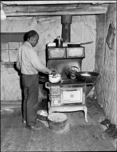 Joshua Spradley, miner, who lives alone in garage house, cooking his meal. He has lived here for four years, pays... - NARA - 540934