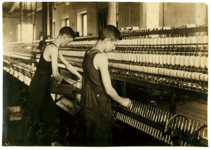 King Philip - Mule Spinning Room. Thomas Nicholls, 54 Kilburn St. Tube boy on the right - doffer on the left. Tube boy 14 years, doffer 16 years. Tube boy slips onto spindle holders. LOC cph.3b33429