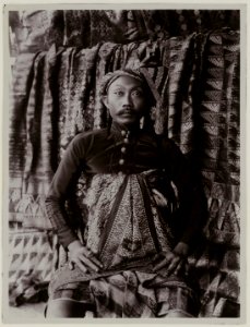 KITLV - 28640 - Kurkdjian, N.V. Photografisch Atelier O. - Soerabaja - Balinese man with a number of woven fabrics in the background - circa 1912