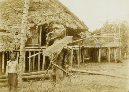 KITLV - 160452 - Demmeni, J. - Hudo (mask for dancer or priest) and a woman in front of a house in the Apokayan, Borneo - 1898-1900
